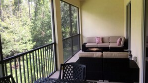 Un balcón con sofá y sillones, un ventilador de techo y vistas a un bosque.