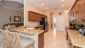 Una cocina moderna con encimeras de granito, armarios de madera, un refrigerador y un comedor con sillas.