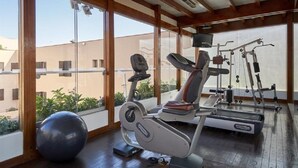 Een sportschool met trainingsapparatuur, grote ramen en uitzicht op gebouwen.