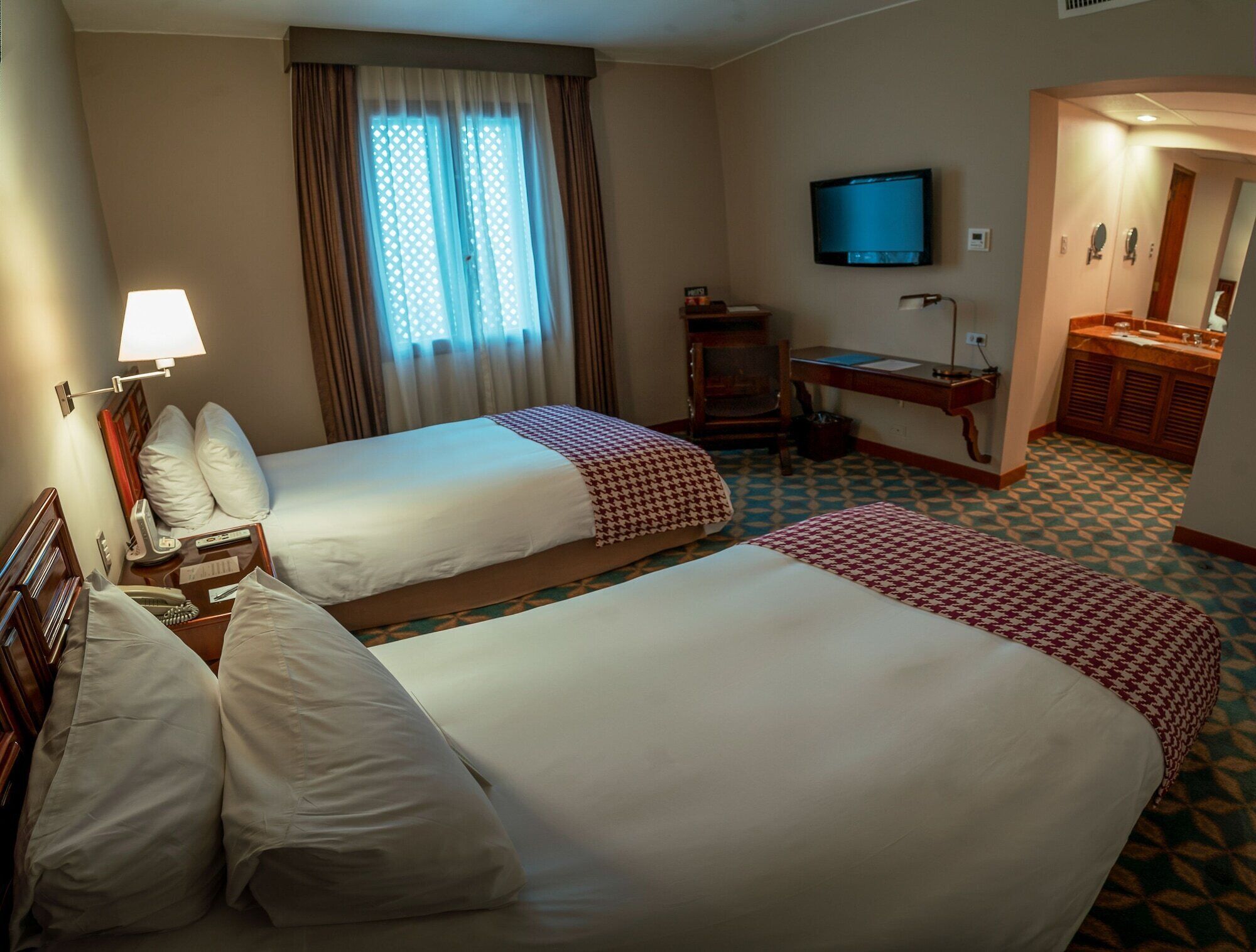 A hotel room with two beds, a TV, a desk, and a bathroom.