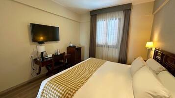 Una habitación de hotel con una cama grande, un escritorio con silla, televisión y una ventana con cortinas.