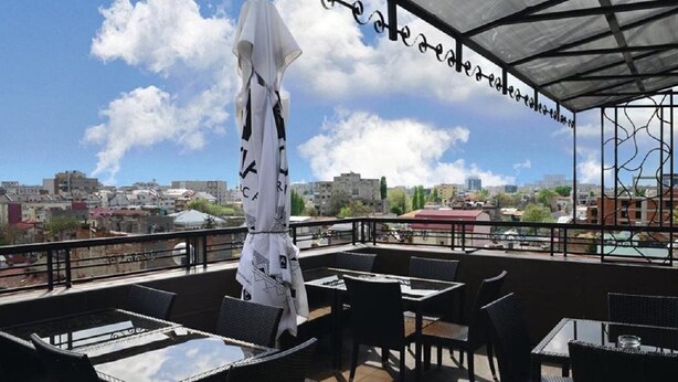 An outdoor patio with tables and chairs, a white umbrella, and a city view in the background. - Razvan (Bucharest)