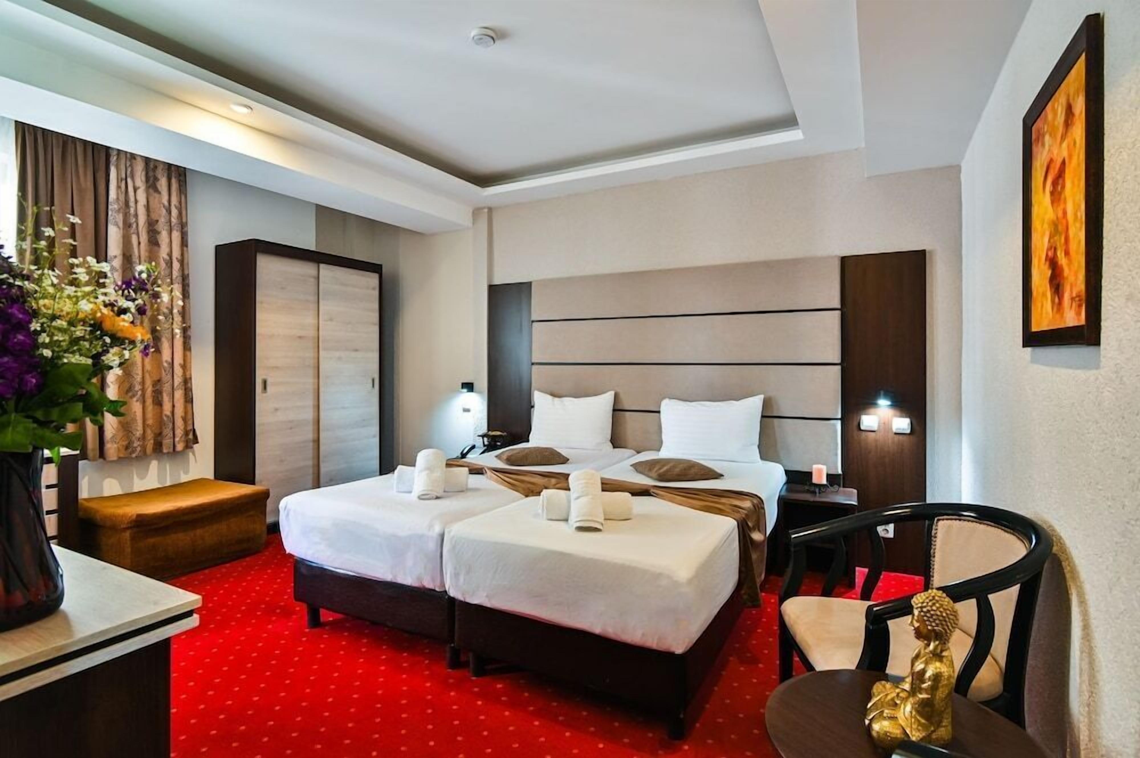 A hotel room with two beds, a desk, a chair, and a small statue.