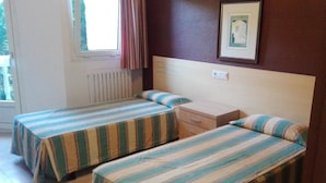 Une chambre avec deux lits simples, une fenêtre avec des rideaux, un radiateur et un tableau encadré au mur.