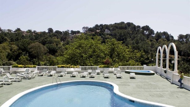 Une piscine avec des chaises longues et une vue sur une colline boisée.