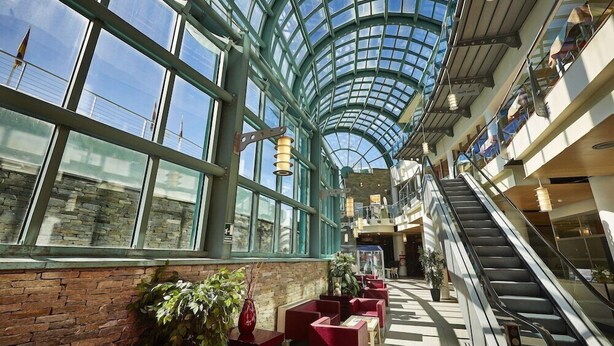 A spacious atrium with a glass ceiling, multiple seating areas, and an escalator.