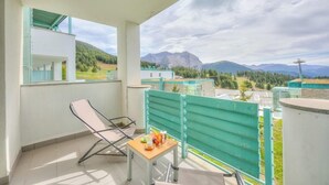 A balcony with a table and chairs, overlooking a mountainous landscape.
