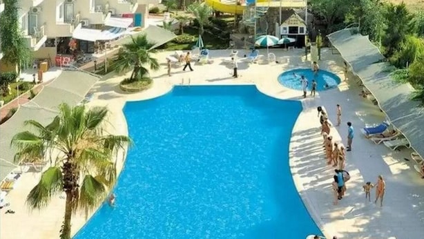 A resort with a large swimming pool, palm trees, and a water slide. - Asrin Beach (Alanya)