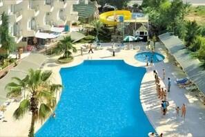 A resort with a large swimming pool, palm trees, and a water slide. - Asrin Beach (Alanya)