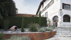 A hotel courtyard with a stone pathway, a metal planter with plants, and a building with the name "Hotel Garnis Chartreuse". - Hotel Chartreuse (Hilterfingen)