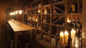A long wooden table with chairs, surrounded by wine racks with bottles and candles. - Hotel Chartreuse (Hilterfingen)