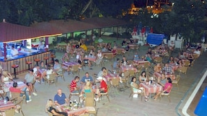 An outdoor dining area with multiple tables and chairs, a bar, and a poolside view. - Doris Aytur (Alanya)