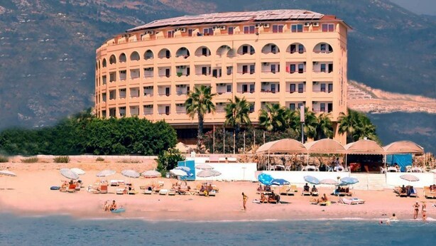 A large hotel with multiple balconies, a beach in front, and palm trees. - Doris Aytur (Alanya)