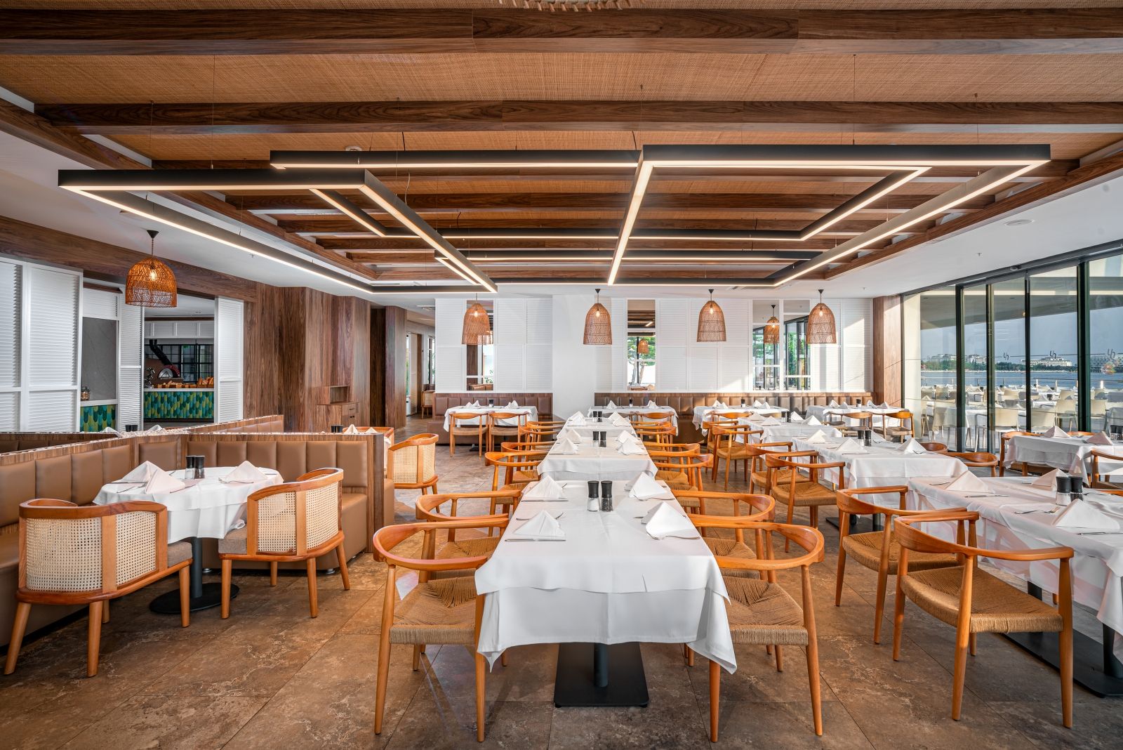 Un restaurante espacioso con mesas largas, sillas de madera y vista al agua.