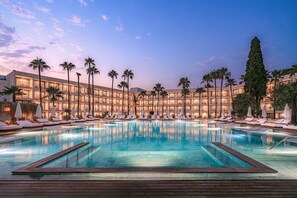 Un hôtel doté d’une grande piscine, de palmiers et d’un immeuble à plusieurs étages avec des balcons.