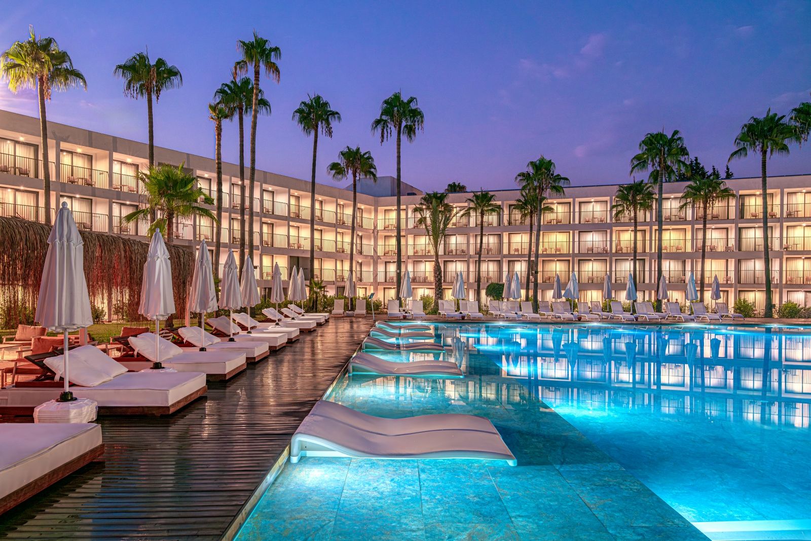 Un hôtel doté d’une piscine, de chaises longues et de palmiers.