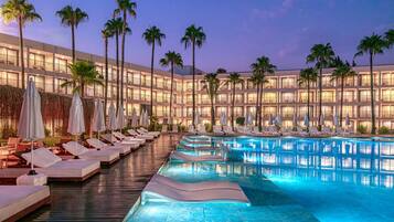 Un hôtel doté d’une piscine, de chaises longues et de palmiers.