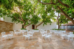 An outdoor patio with white chairs arranged in rows, surrounded by large trees and a stone floor. - Yalihan Aspendos Hotel (Alanya)