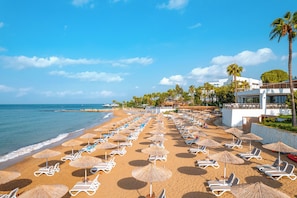 A beach with sun loungers and umbrellas, a building with a balcony, and palm trees. - Yalihan Aspendos Hotel (Alanya)