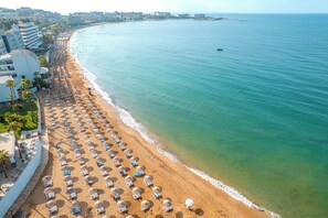 A beach with rows of sun loungers and umbrellas, a clear view of the ocean, and buildings along the coastline. - Yalihan Aspendos Hotel (Alanya)