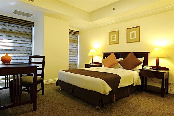 A hotel room with a bed, bedside tables, a chair, a table, and a window with blinds. - Somerset Salcedo Makati (Makati)