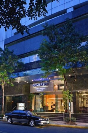 Un hotel moderno con fachada de vidrio, una entrada visible y un coche estacionado frente a él.