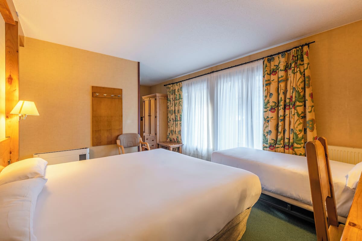 A hotel room with two beds, a chair, a desk, and a mirror.