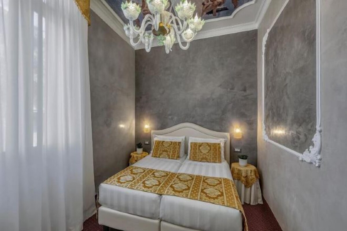 A bedroom with a large bed, a chandelier, and a nightstand.