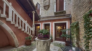 A courtyard with a stone staircase, a central planter with plants, and a metal table with chairs. - Pausania Hotel (Venice)