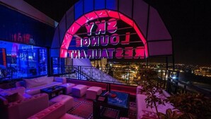 Un área de lounge en la azotea con un letrero de neón que dice "SNY LON" y "LOUNGE", que ofrece vistas de la ciudad y muebles modernos.