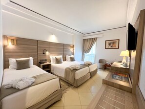 Habitació d'hotel amb dos llits, escriptori, cadira, televisió i finestra amb cortines.