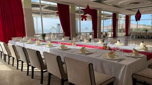 A long dining table set for a meal with white tablecloths, red accents, and a view of the sea through large windows. - Adriatik Hotel, BW Premier Collection (Durrës)