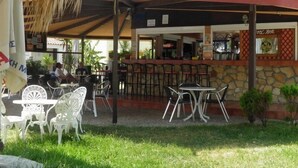 An outdoor cafe with tables and chairs, a stone wall, and a covered seating area. - Ammes Hotel & Apartments (Kefalonia)