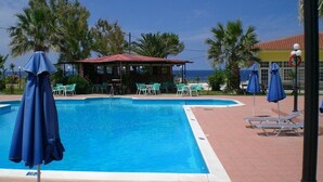 A swimming pool with lounge chairs and umbrellas, a covered seating area, and palm trees. - Ammes Hotel & Apartments (Kefalonia)