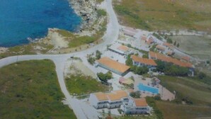 An aerial view of a coastal resort with a winding road, multiple buildings, and a swimming pool. - Ammes Hotel & Apartments (Kefalonia)
