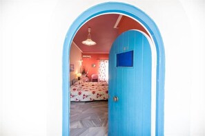 A room with a blue door, a bed with floral bedding, a red wall, and a hanging light fixture. - Ammes Hotel & Apartments (Kefalonia)