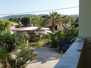 A residential area with houses, a parked car, and a balcony overlooking a garden with palm trees. - Ammes Hotel & Apartments (Kefalonia)
