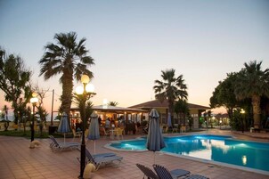 Un área junto a la piscina con sillones de descanso, sombrillas y un bar.
