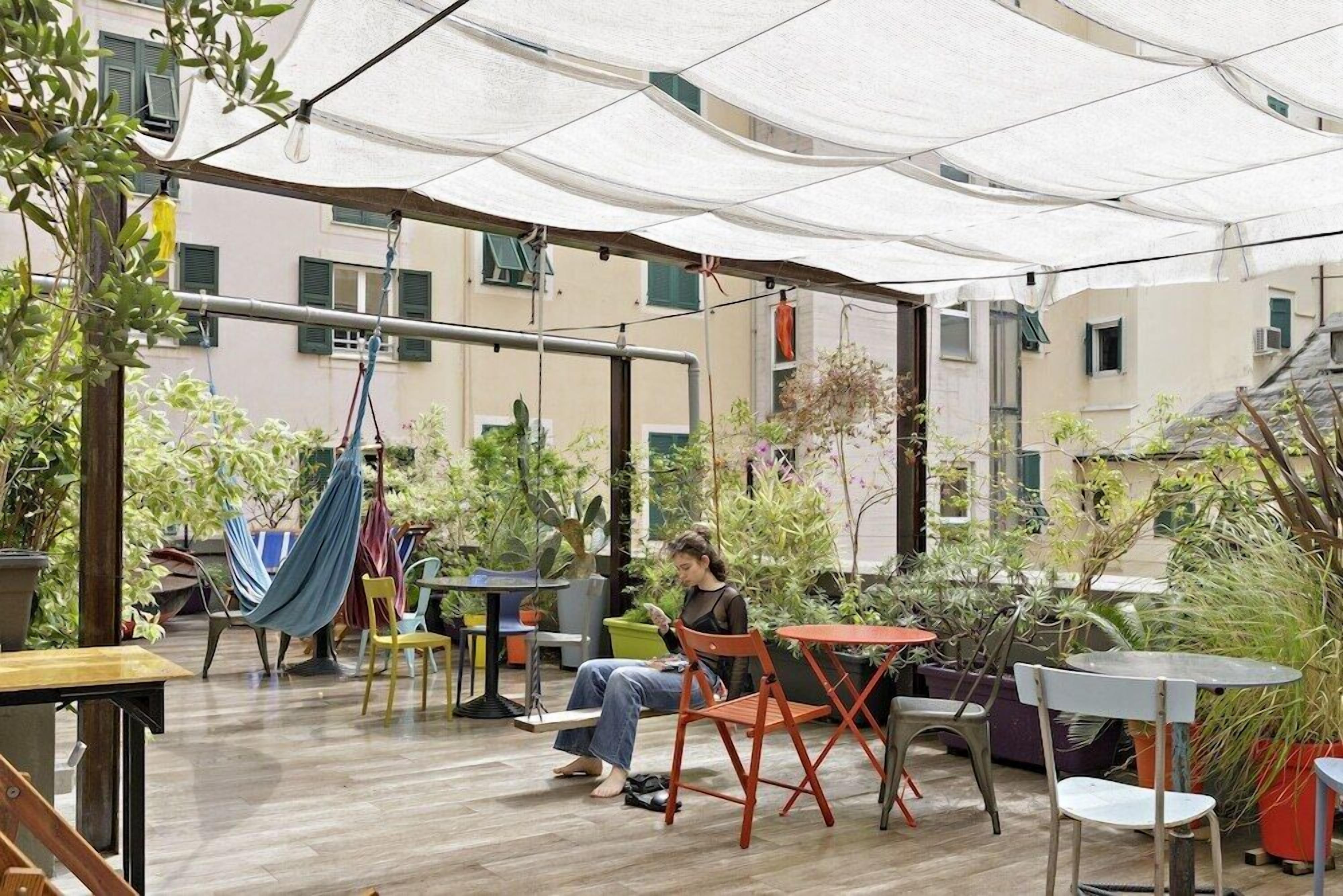 An outdoor patio area with tables and chairs, surrounded by potted plants and a hanging hammock.