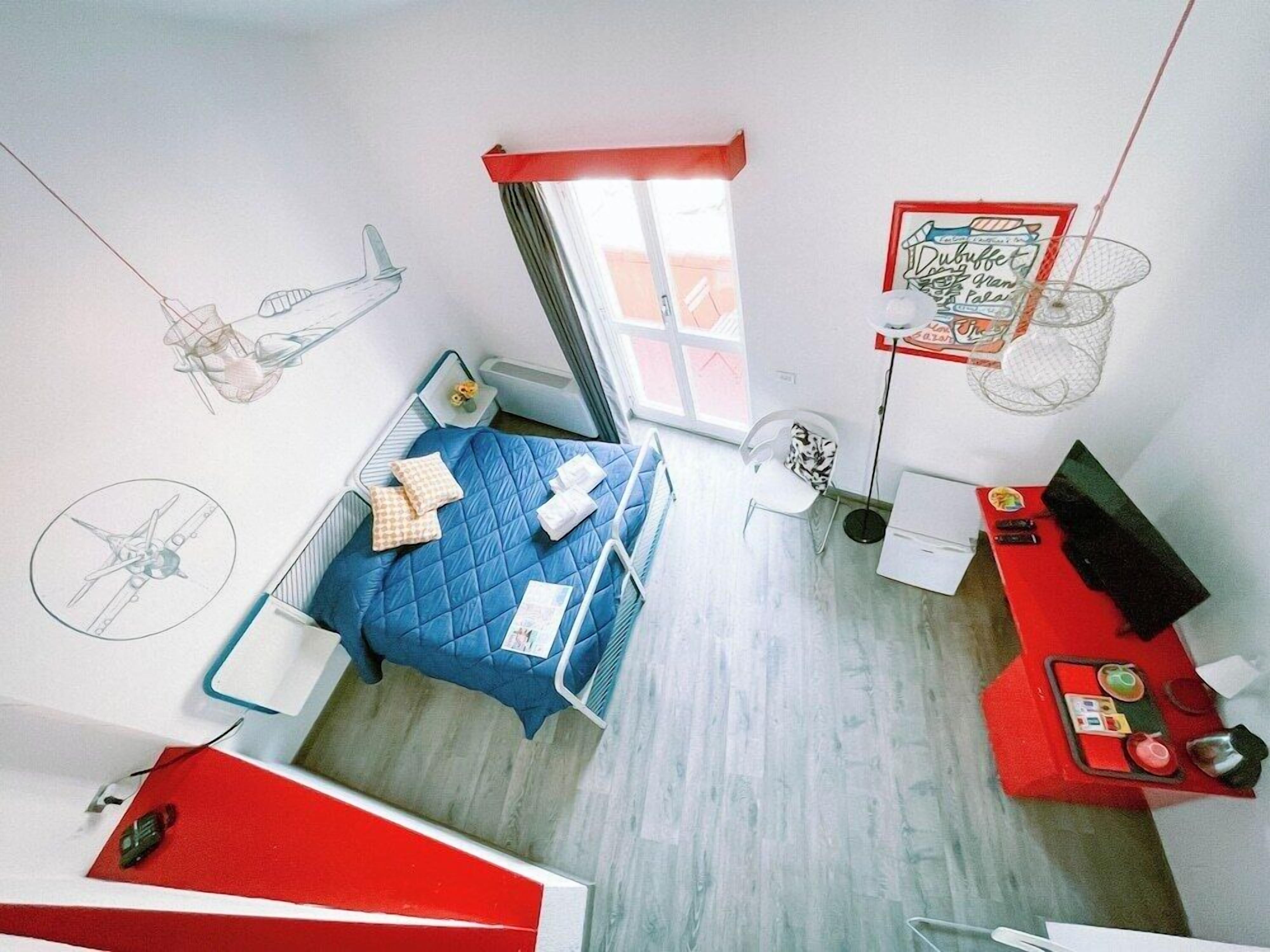 Una habitación con cama, escritorio, silla, ventana y ventilador de pared.