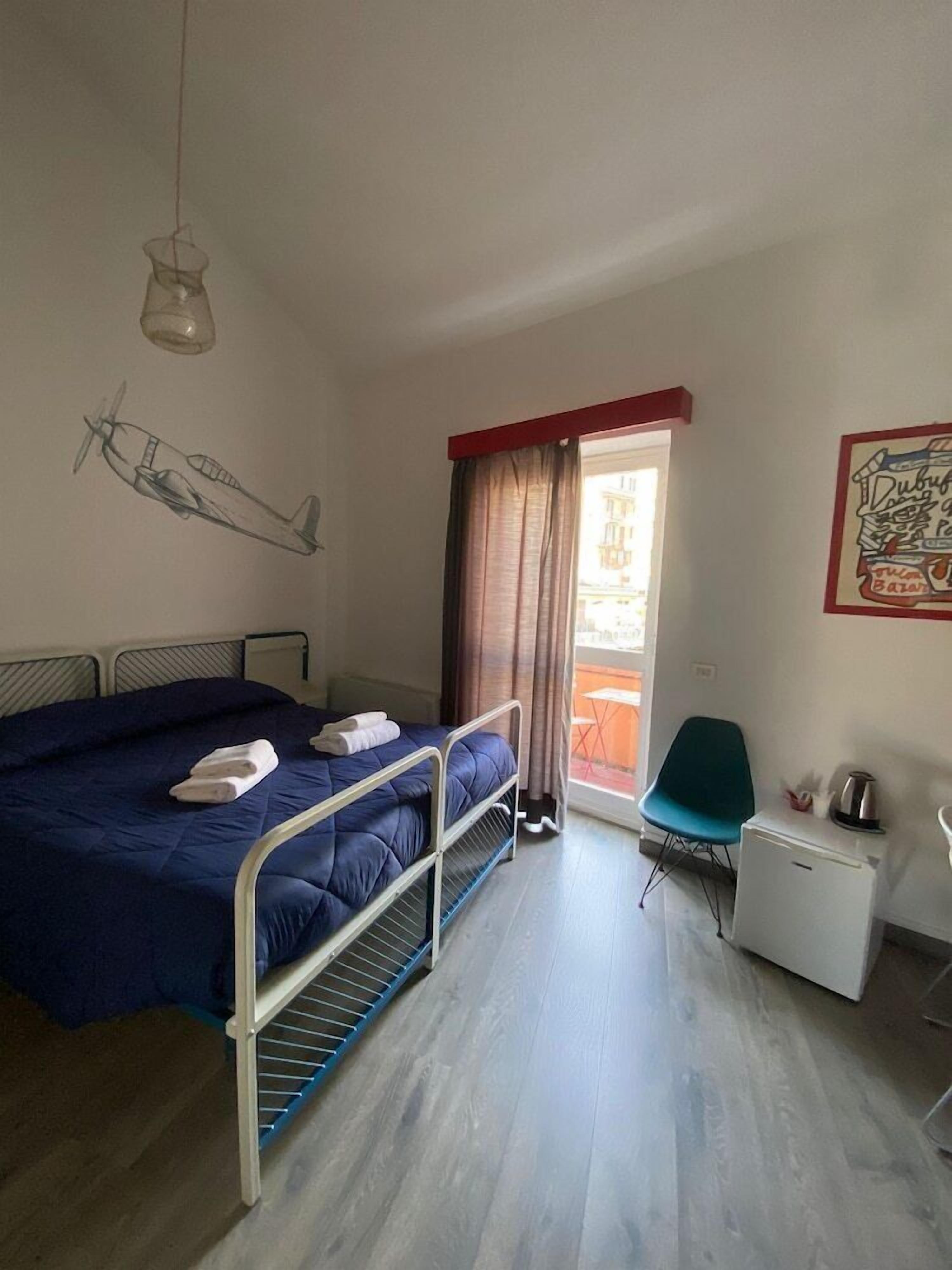 A bedroom with a bed, a desk, a chair, a window with curtains, and a wall art piece.