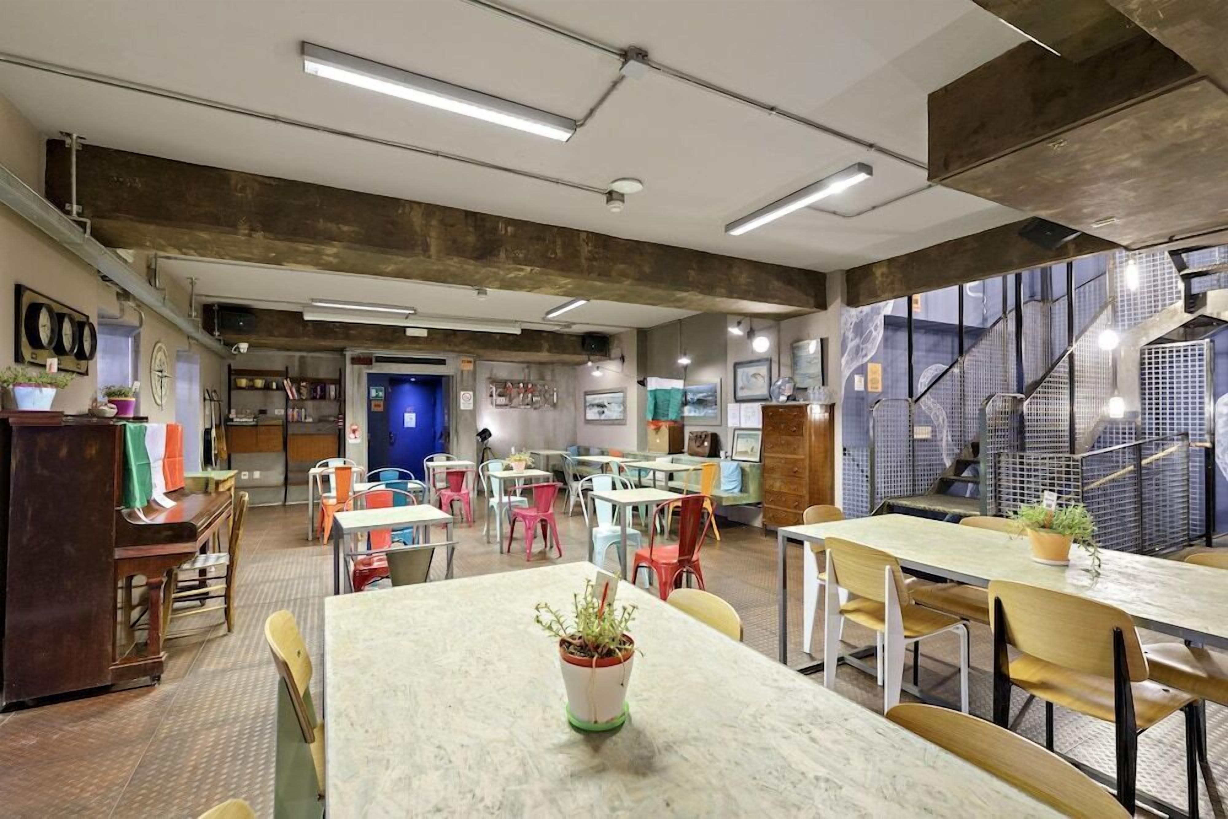 A modern dining area with tables and chairs, a staircase, and a view of the city.