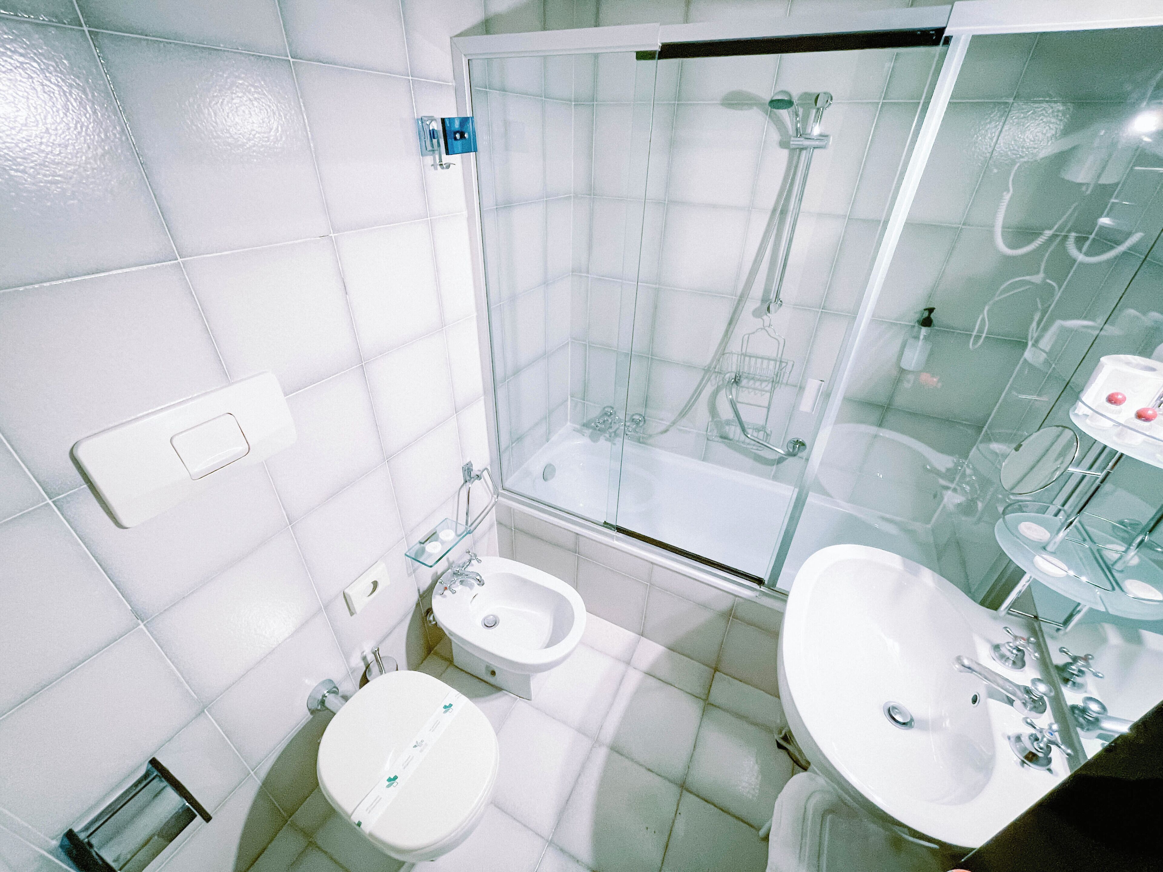 A bathroom with a glass-enclosed shower, two sinks, and a toilet.