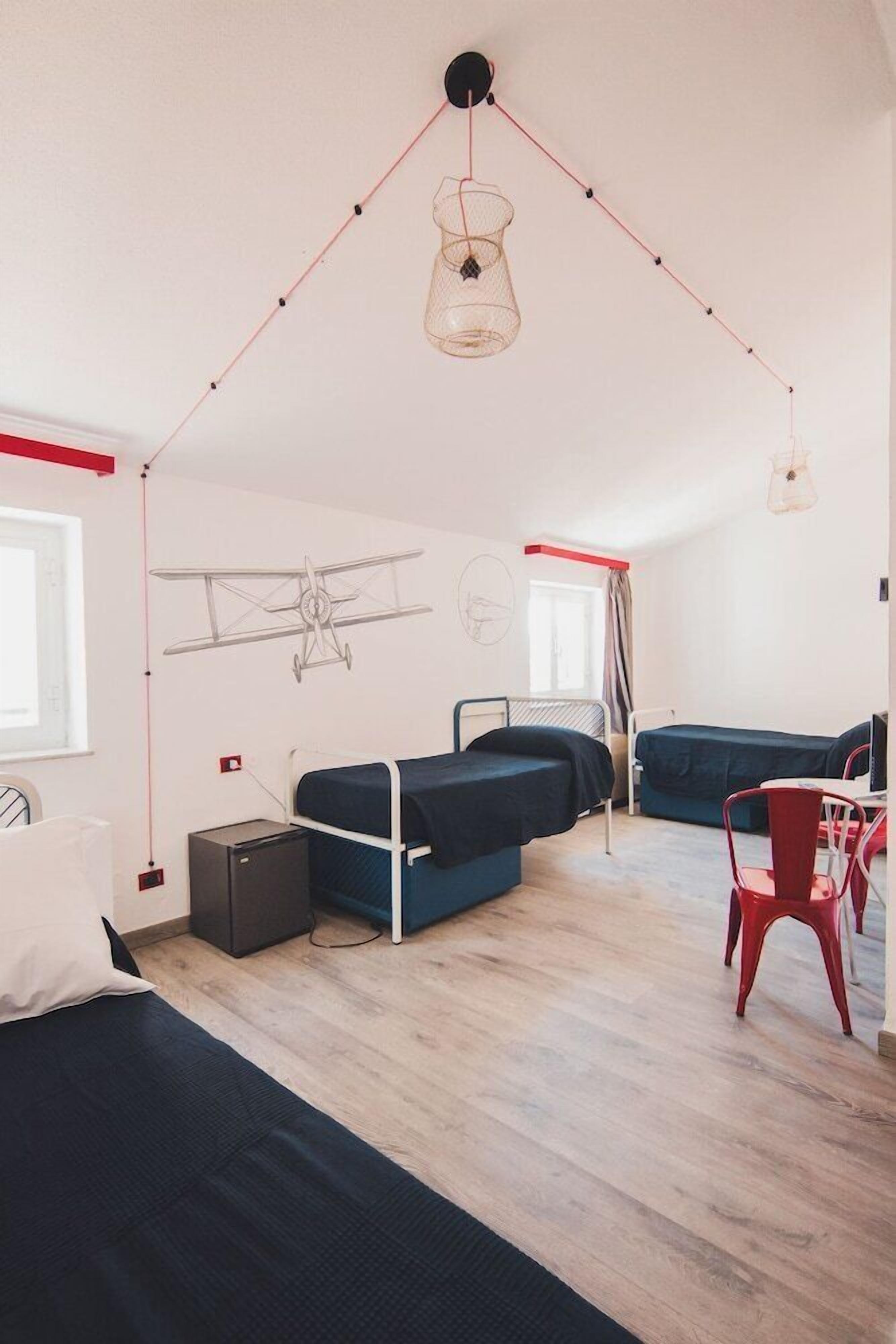 A compact room with bunk beds, a desk, and a chair. There is a hanging light fixture and a window with curtains.