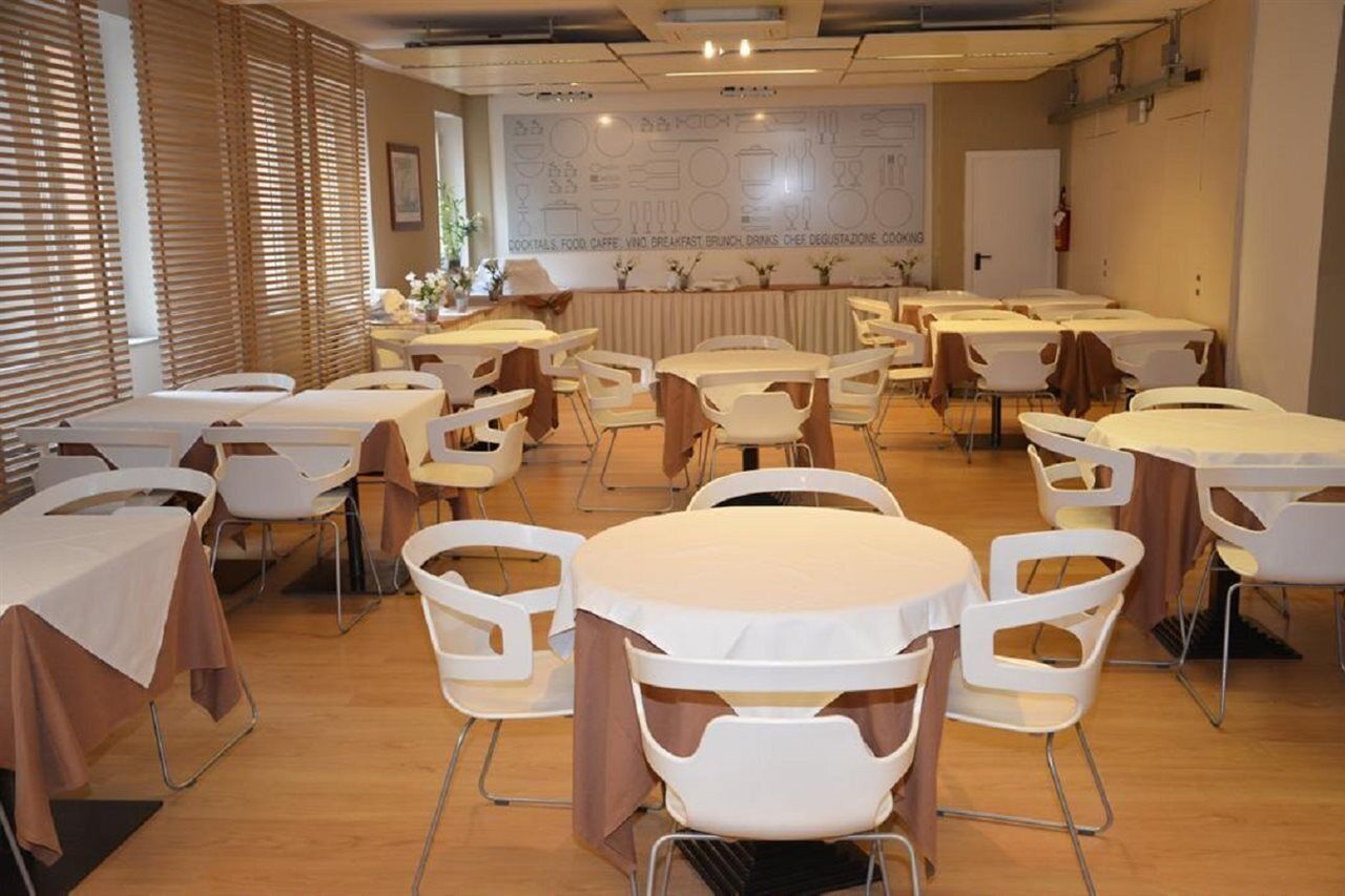 A conference room with multiple tables and chairs, a large wall with a menu board, and a window with blinds.