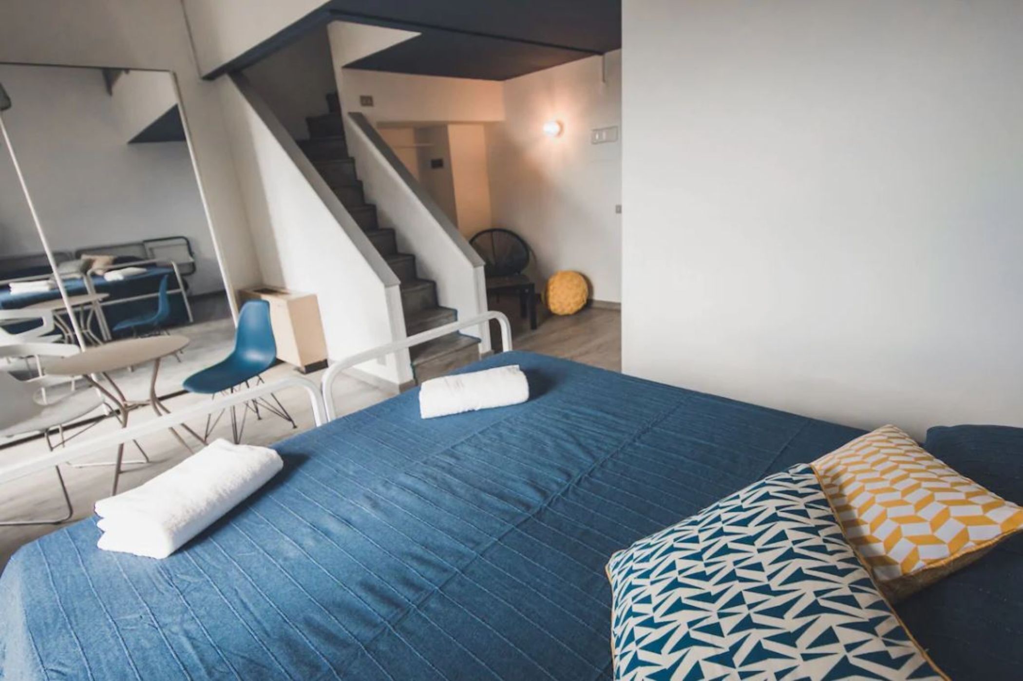 A modern hotel room with a large bed, a chair, a desk, and a staircase leading to another area.