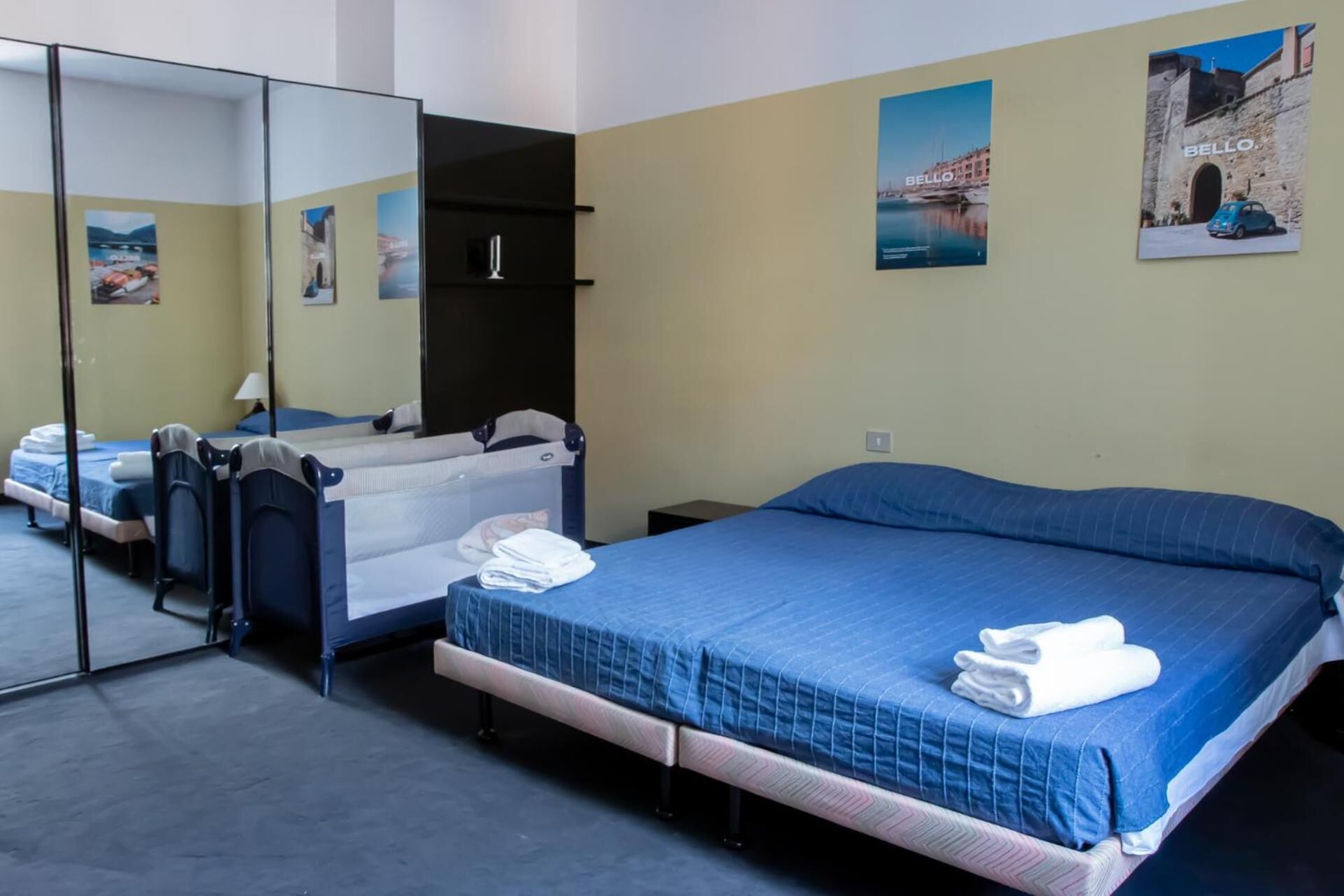 A bedroom with a bed, a crib, a mirror, and a wall with posters.
