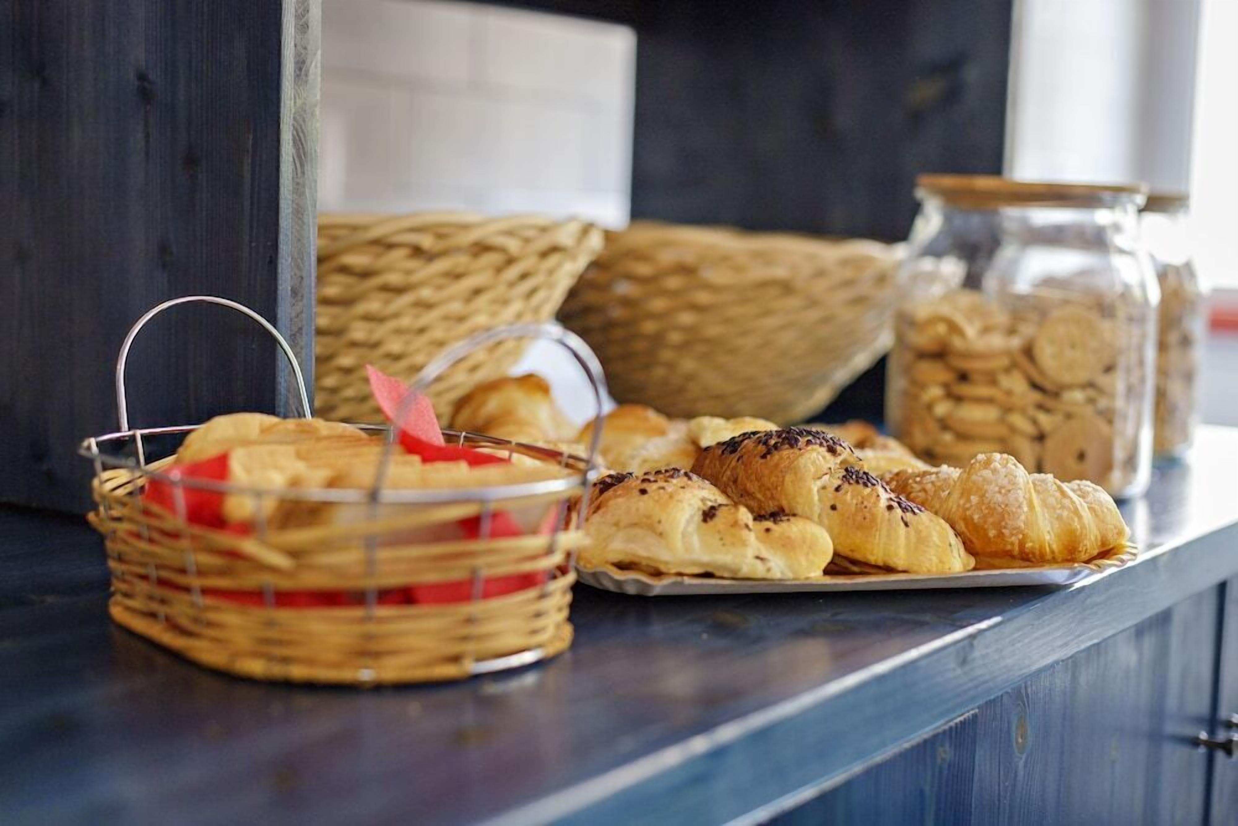 A wooden table with a basket of cookies, a jar of cookies, and a tray of croissants.