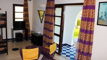 A room with a checkered floor, a television, a desk, two rocking chairs, and purple curtains.