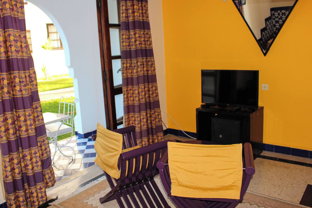 A room with a yellow wall, a television, a purple chair, and a patterned curtain.